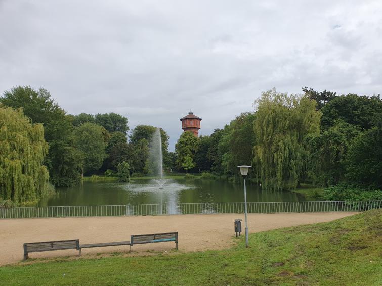 Ein See mit einer Föntane. Im Hintergrund ist ein Turm zu sehen.